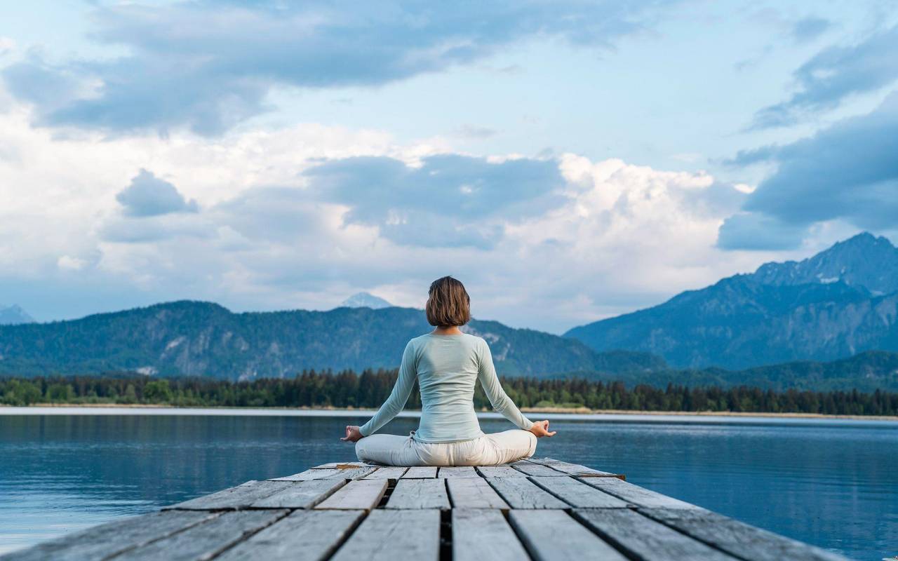 Eine Frau sitzt auf einem Steg und meditiert