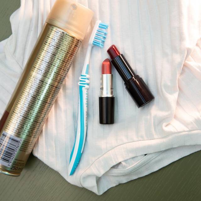 Lippenstift, Haarspray und eine Zahnbürste liegen auf einem Shirt