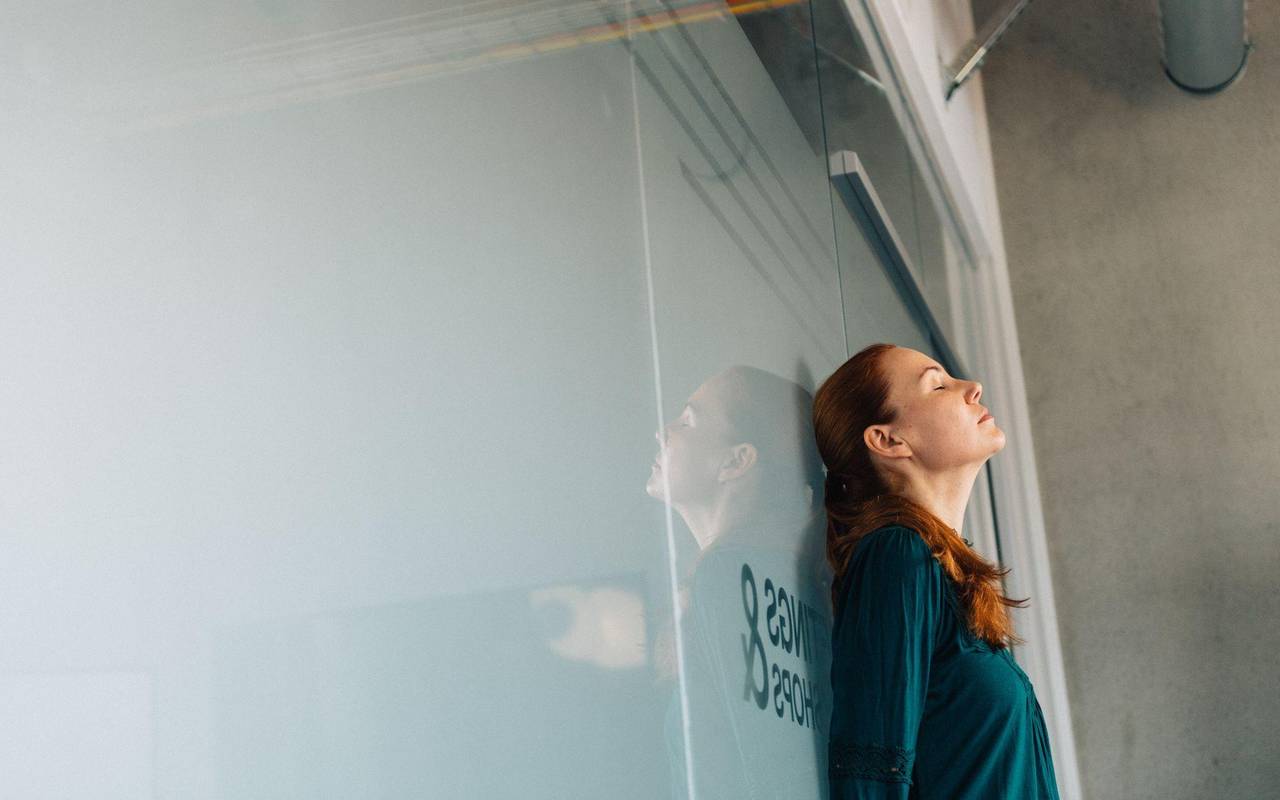 Eine Frau lehnt erschöpft an einer Glaswand im Büro