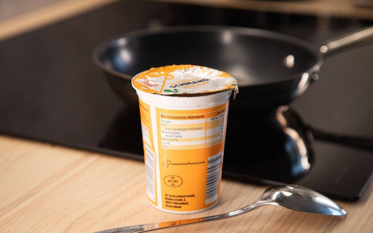 Ein Becher Schmand steht neben einer Pfanne