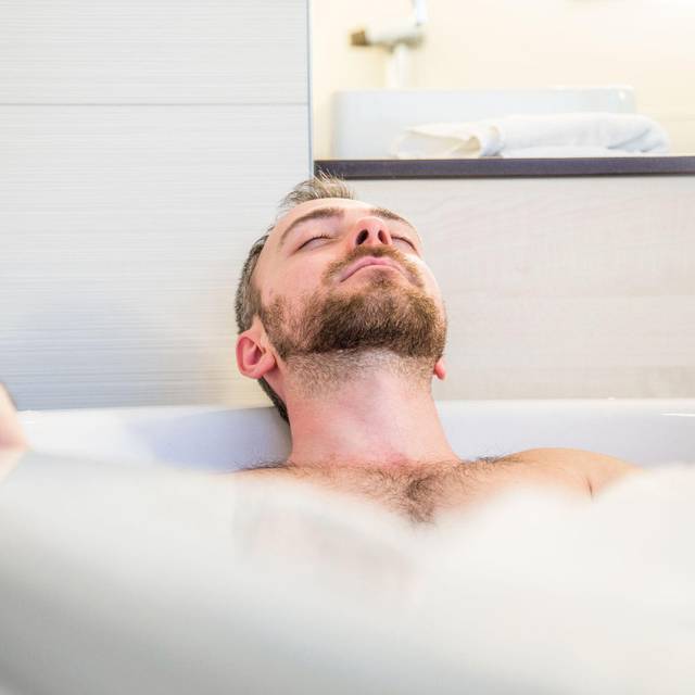 Ein Mann liegt mit geschlossenen Augen in der Badewanne