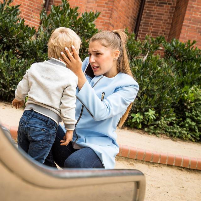 Mutter hält auf dem Spielplatz besorgt den Kopf ihres Kindes