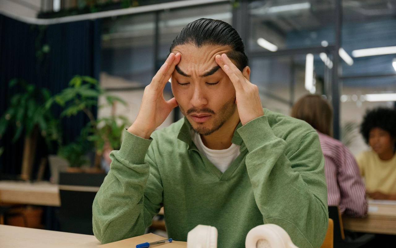 Ein Mann fasst sich an die Schläfen in einem Großraumbüro