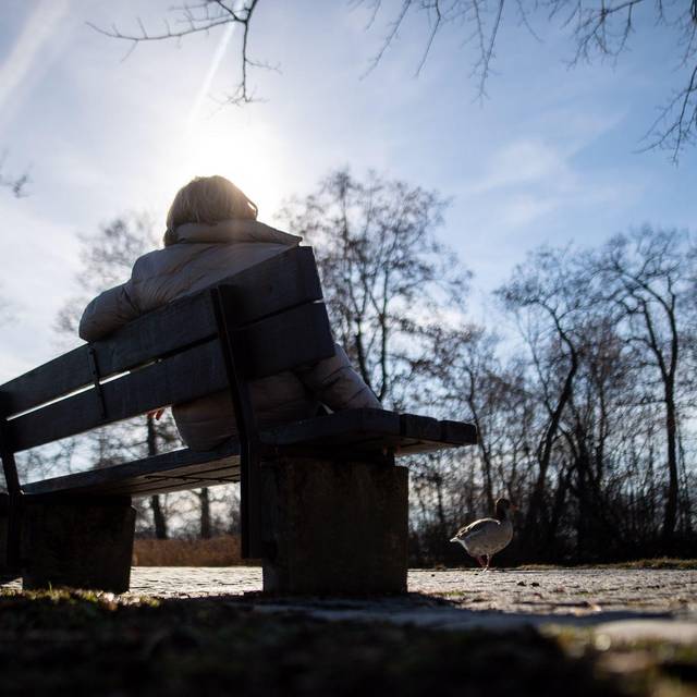 Eine Frau sitzt neben kahlen Bäumen in der Sonne