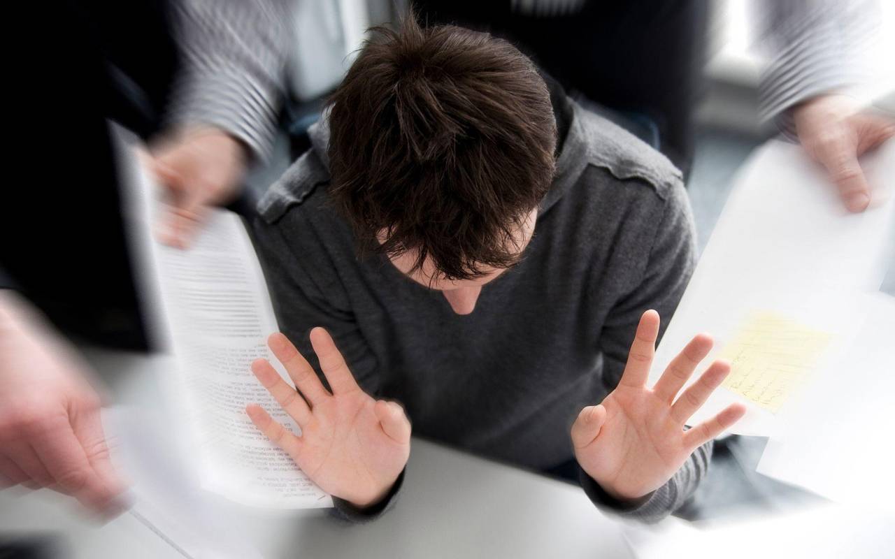 Mann mit hoher Arbeitsbelastung hebt im Büro abwehrend die Hände