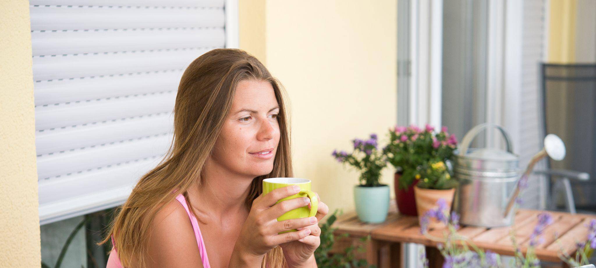 Frau sitzt auf einem Balkon und trinkt Kaffee